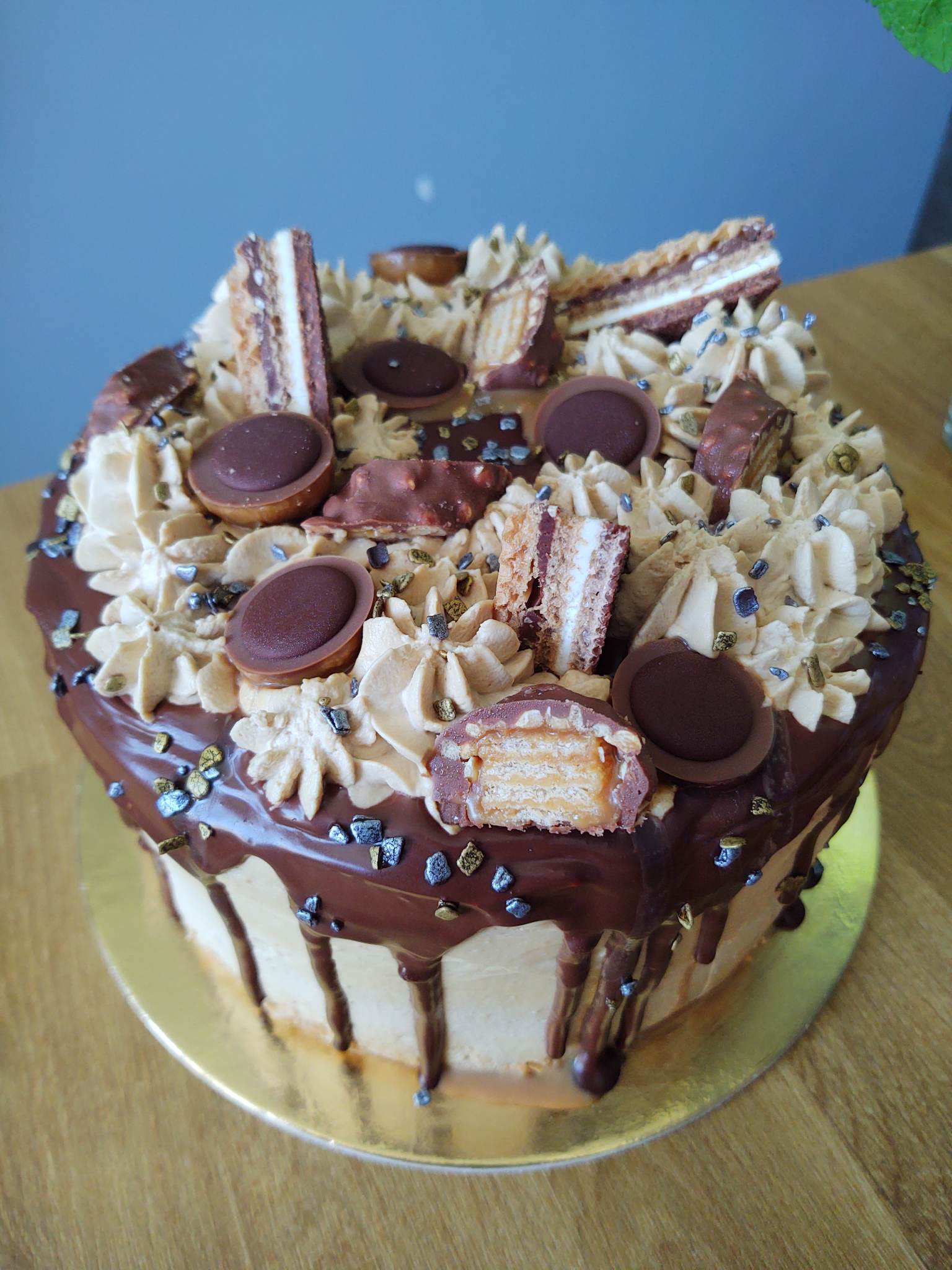 Dekorowany tort z kremem, polewą czekoladową, batonikami i okrągłymi czekoladkami na złotym podkładzie, widzoczny przekrój jednego z batoników.