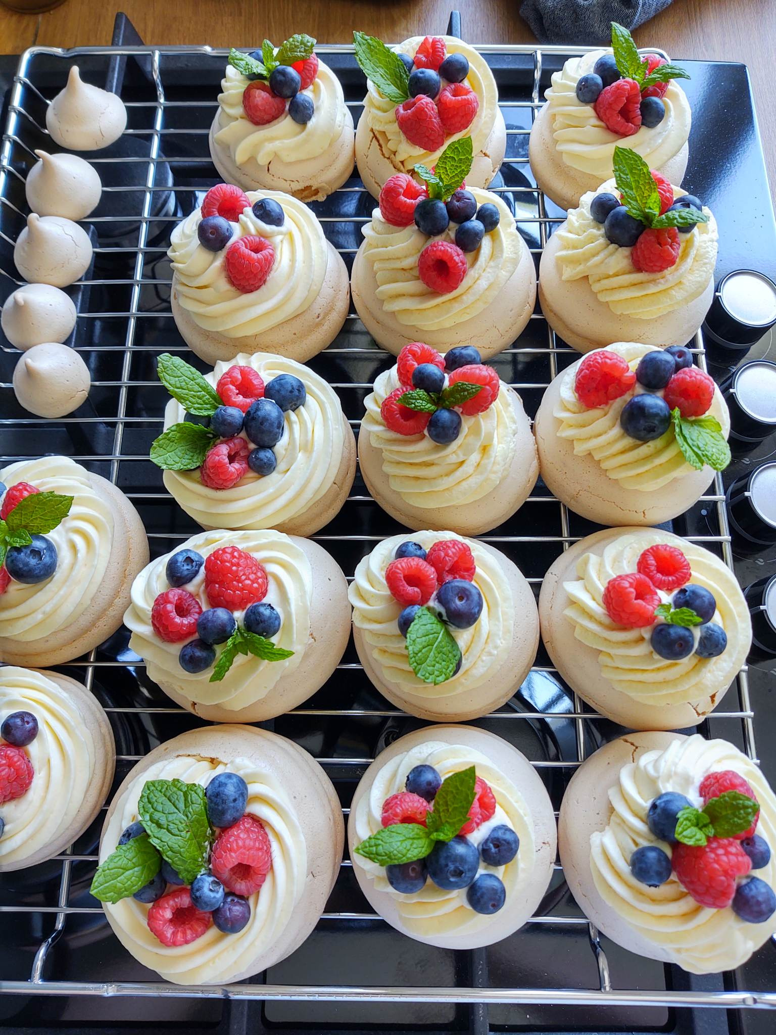 Bezy z kremem i owocami: maliny, borówki i listki mięty, ułożone na metalowej kratce.