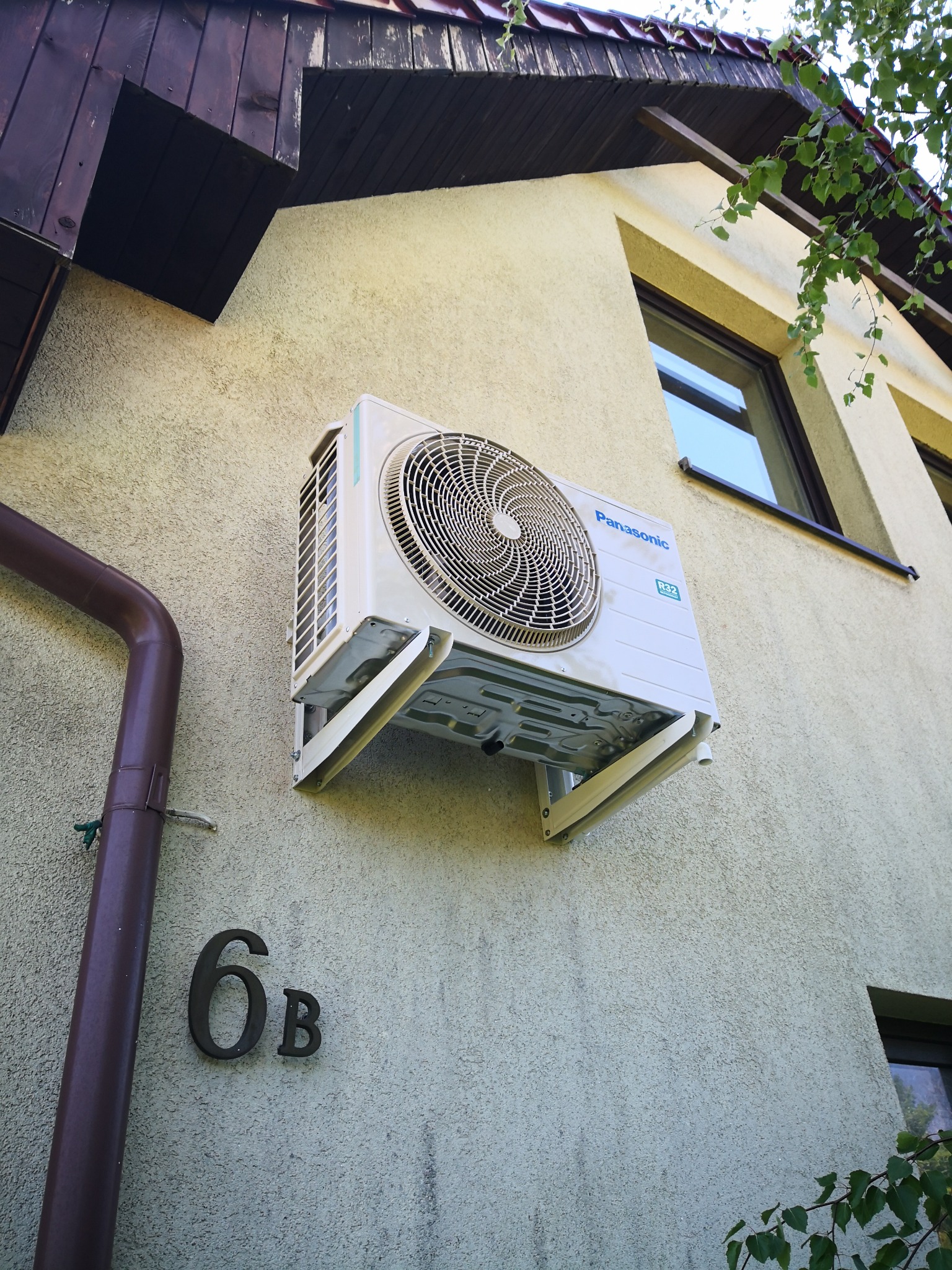 Zewnętrzna jednostka klimatyzacji Panasonic zamontowana na elewacji budynku z numerem 6b, widoczny fragment rynny i okno.