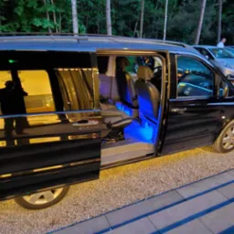 Czarny van z otwartymi drzwiami, podświetleniem LED wewnątrz i zasłonami w oknach, stojący na żwirowym parkingu.