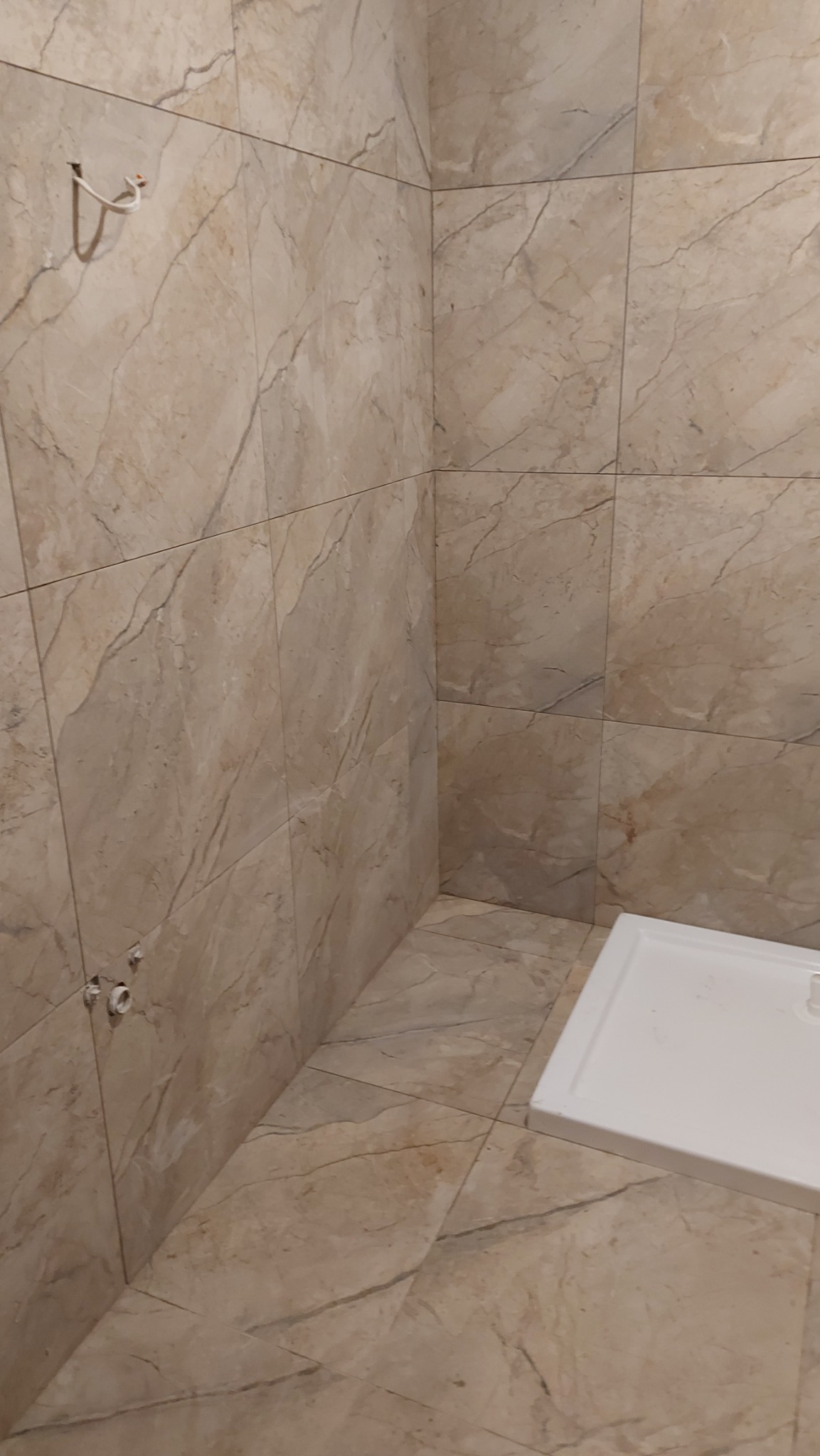 Wykończona łazienka w Szczecinie z beżowymi płytkami imitującymi marmur na ścianach i podłodze. Widoczny brodzik i przygotowane przyłącze wodne.