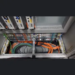 Wnętrze szafy sterowniczej z uporządkowanymi kablami w różnych kolorach, widoczne moduły elektroniczne i złącza.