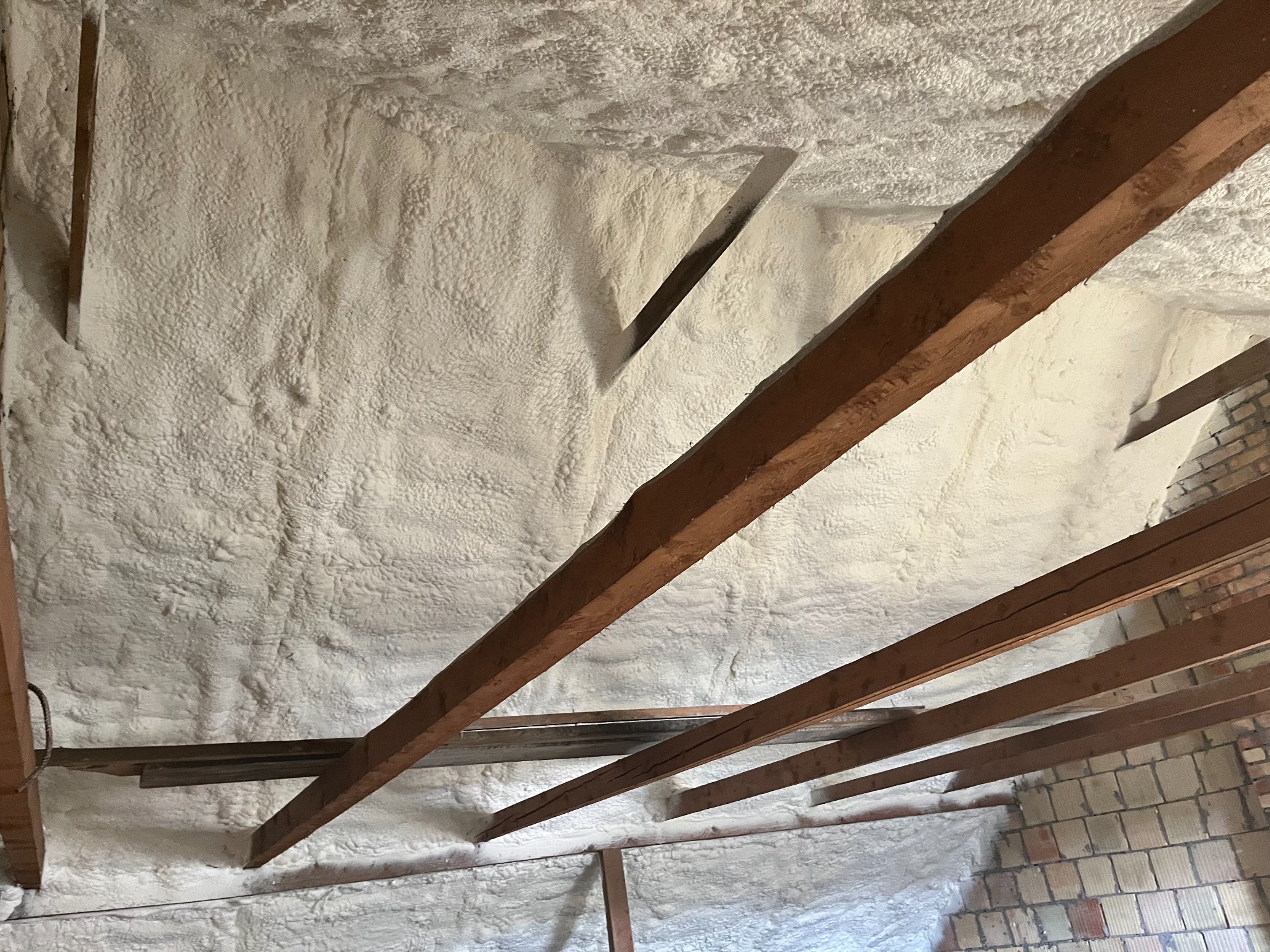 Poddasze z widoczną drewnianą konstrukcją i grubą warstwą jasnej, natryskowej izolacji termicznej o nieregularnej fakturze.