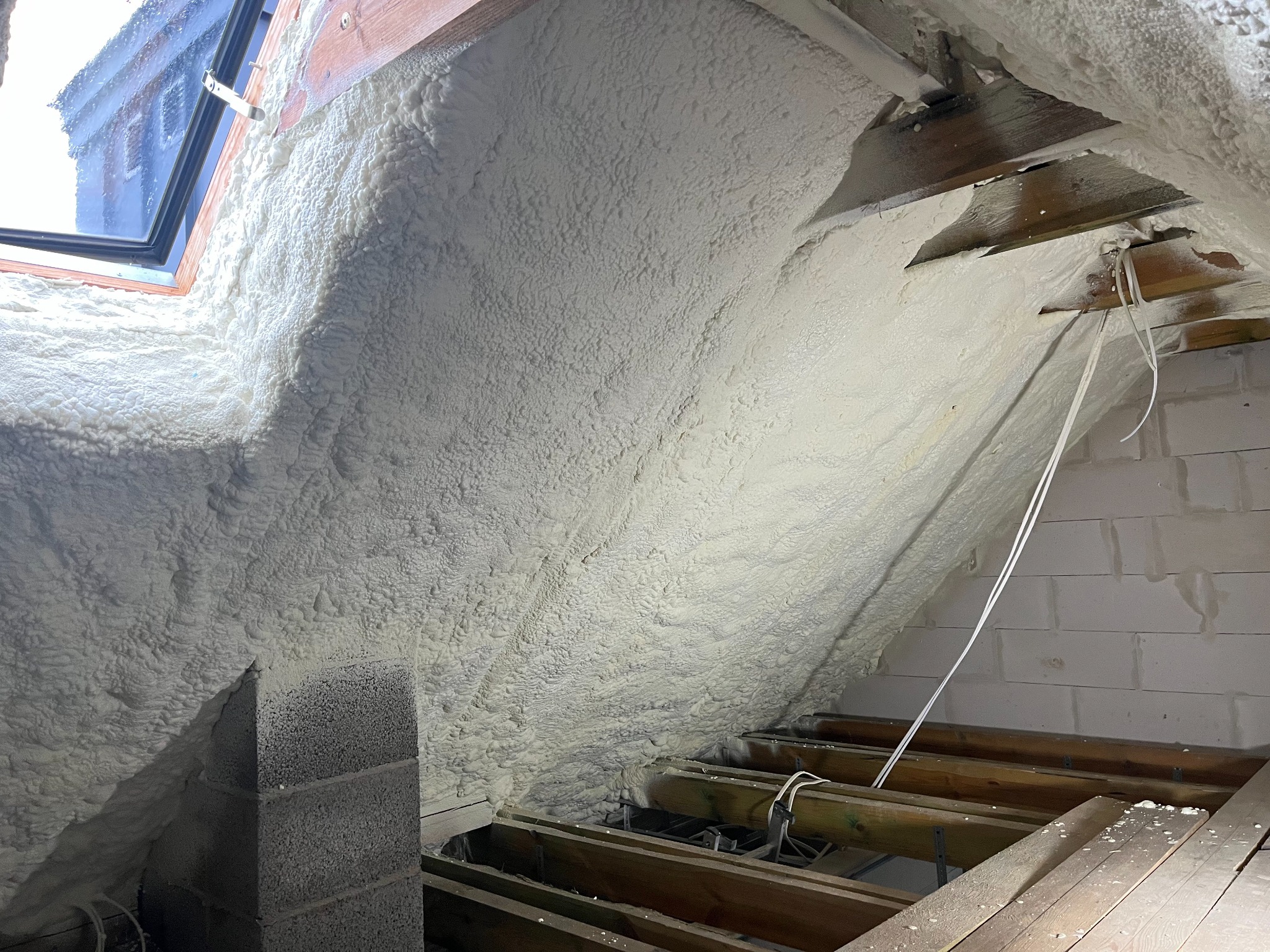 Poddasze po natrysku izolacji piankowej, widoczne drewniane elementy konstrukcyjne i okno dachowe.