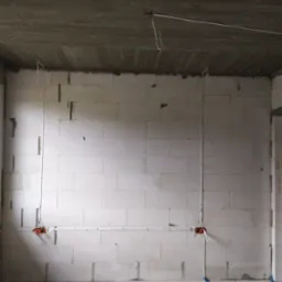 Surowy stan: instalacja elektryczna w trakcie montażu w pomieszczeniu z surowymi ścianami z betonu komórkowego, widoczne kable w peszlach i puszki instalacyjne.