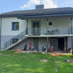 Piotr-Cars - Dwukondygnacyjny dom z szarymi metalowymi schodami zewnętrznymi i balustradą. Na trawniku narzędzia i farby, sugerujące prace wykończeniowe.