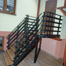 Wnętrze z zamontowanymi schodami metalowymi o drewnopodobnych stopniach i czarnej, minimalistycznej balustradzie. Widoczne elementy konstrukcji drewnianej.