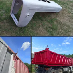 Element karoserii pojazdu w szarym podkładzie na trawie, obok fragmenty odnowionej i odnawianej skrzyni ładunkowej samochodu ciężarowego.