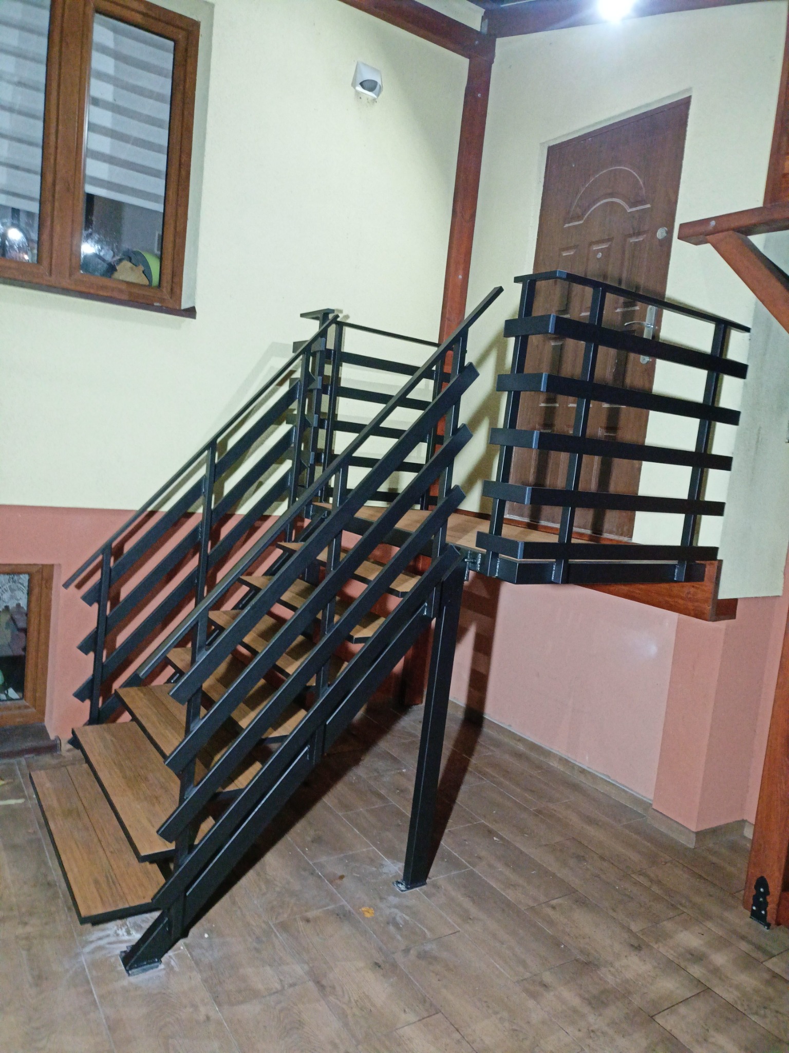 Wnętrze z zamontowanymi schodami metalowymi o drewnopodobnych stopniach i czarnej, minimalistycznej balustradzie. Widoczne elementy konstrukcji drewnianej.