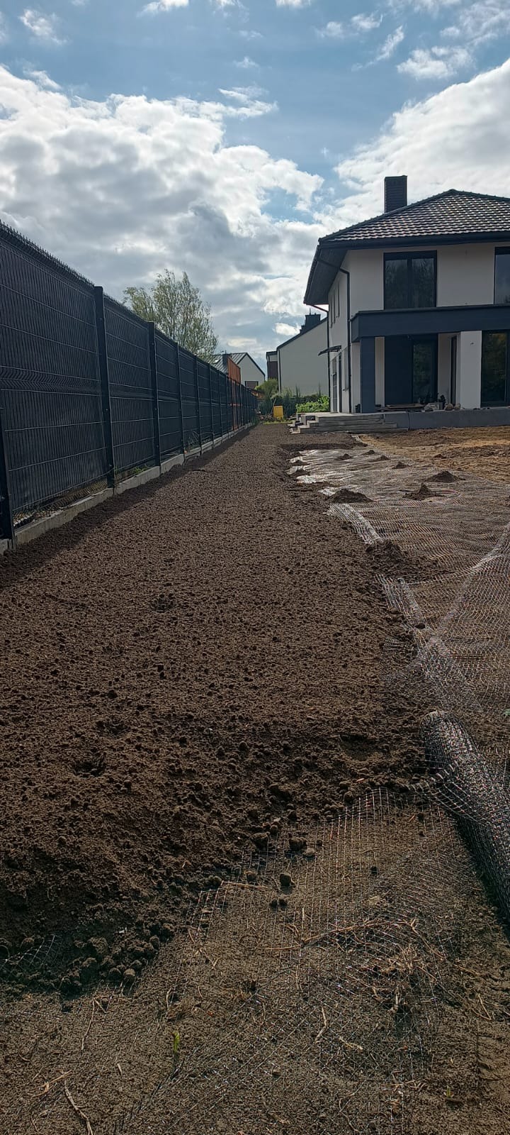 Przygotowanie terenu pod trawnik z rolki: wyrównana ziemia, siatka zabezpieczająca, nowoczesne ogrodzenie panelowe i dom w tle. Widok z perspektywy ziemi.