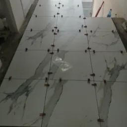 Układanie wielkoformatowych płytek imitujących marmur z użyciem klipsów poziomujących, widoczne fugi i poziomica w tle.