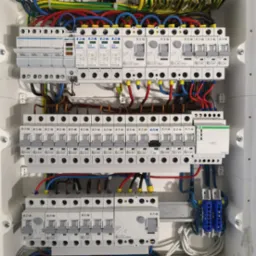 Otwarta skrzynka rozdzielcza z zainstalowanymi bezpiecznikami, przewodami i listwami zaciskowymi; widoczne marki Eaton i Hager.