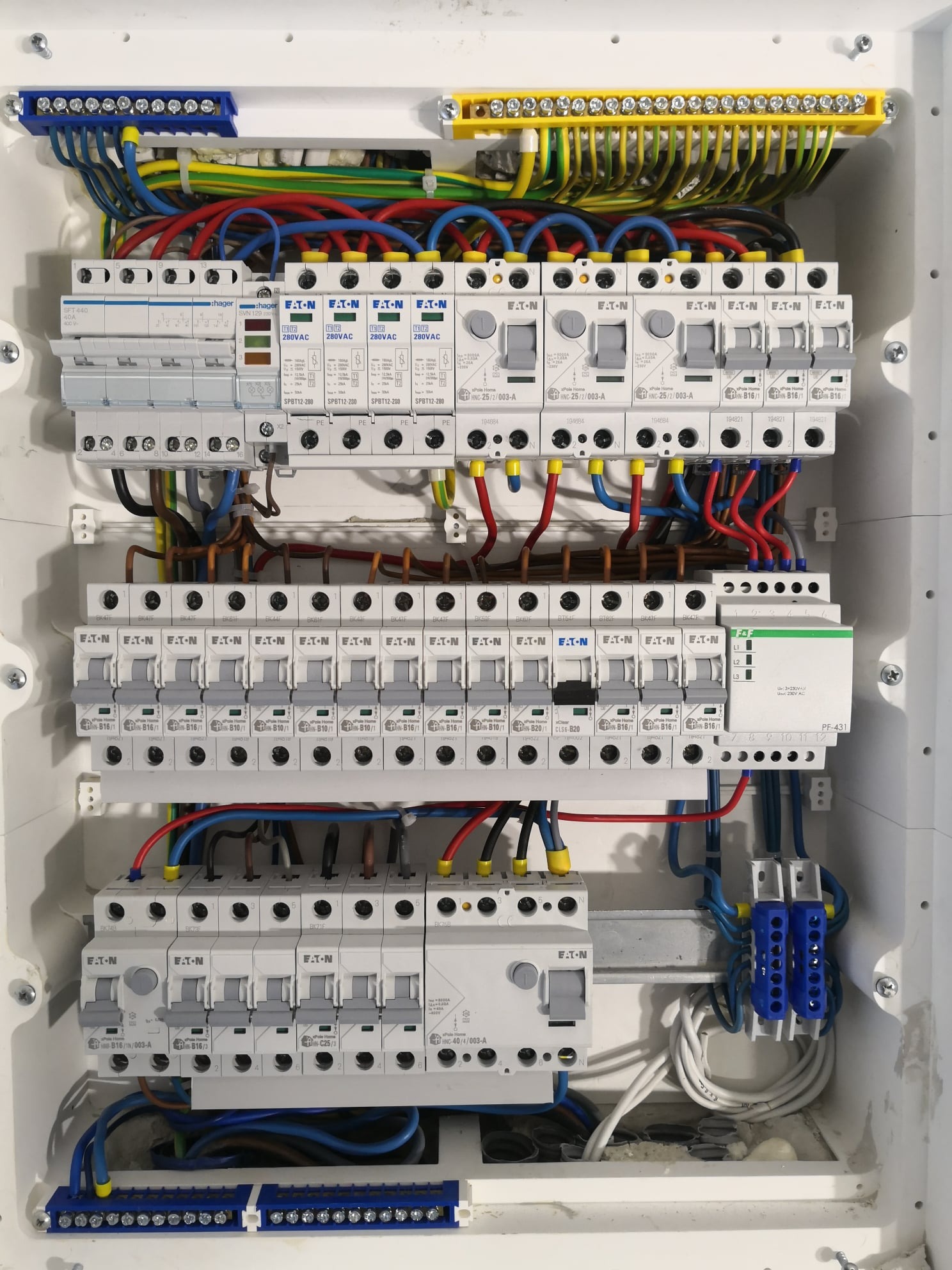 Otwarta skrzynka rozdzielcza z zainstalowanymi bezpiecznikami, przewodami i listwami zaciskowymi; widoczne marki Eaton i Hager.