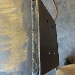 Metalowa konstrukcja skrzynkowa z widocznym, precyzyjnym szwem spawalniczym na krawędzi, z otworami na śruby.