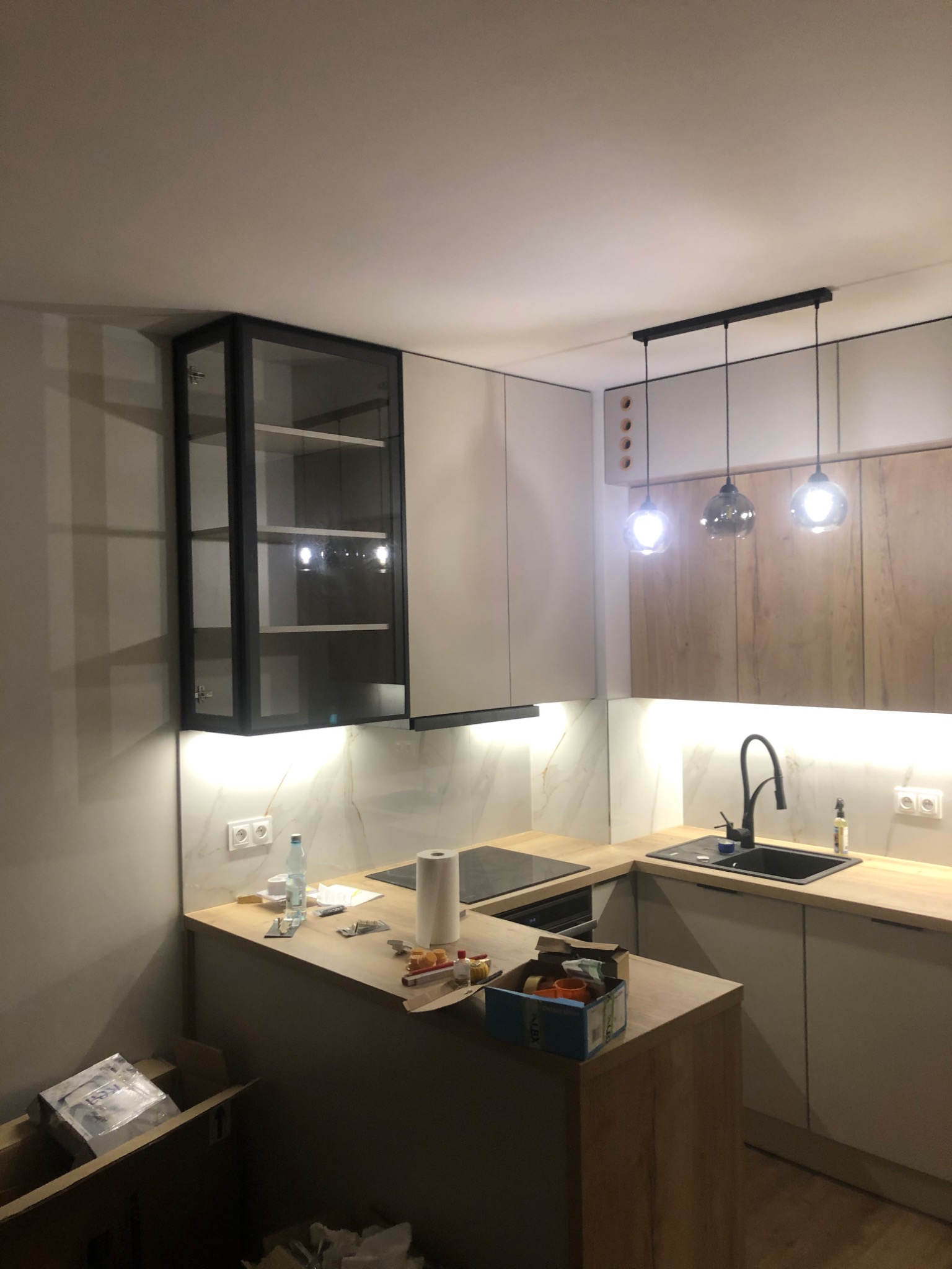 Niedokończona kuchnia w Złotowie z drewnianym blatem, widoczne kartony i narzędzia, szklana szafka wisząca i trzy szklane lampy wiszące.