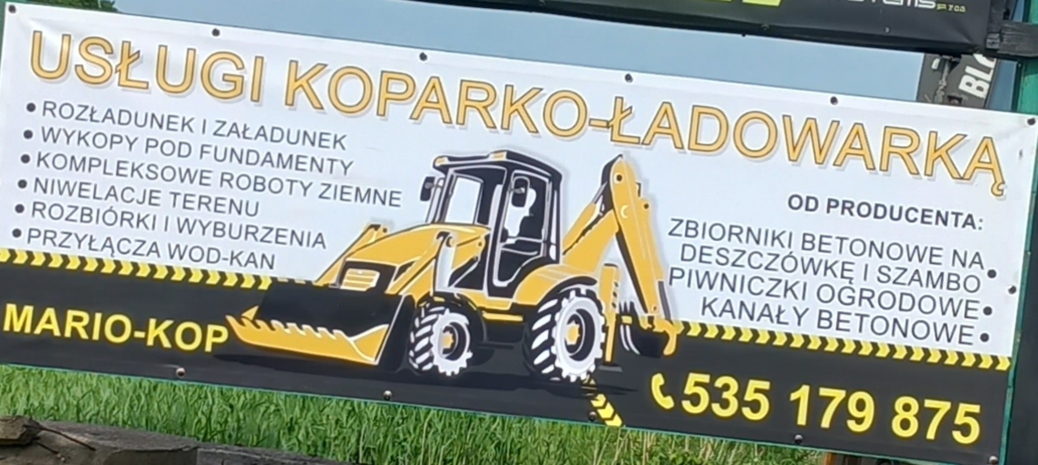 Baner reklamowy firmy Mario-Kop oferującej usługi koparko-ładowarką, wykopów pod fundamenty, niwelacji terenu, rozbiórek i wyburzeń, zbiorników betonowych na deszczówkę i szamba, z numerem telefonu...