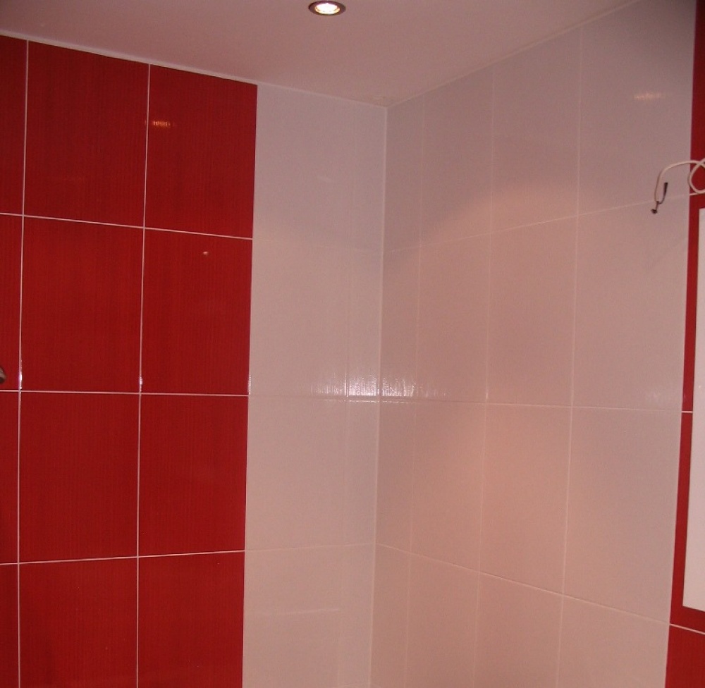 Wykończona łazienka z czerwonymi i białymi błyszczącymi płytkami ułożonymi na ścianach pod kątem prostym, oświetlenie sufitowe typu halogen. Widoczne kable elektryczne.