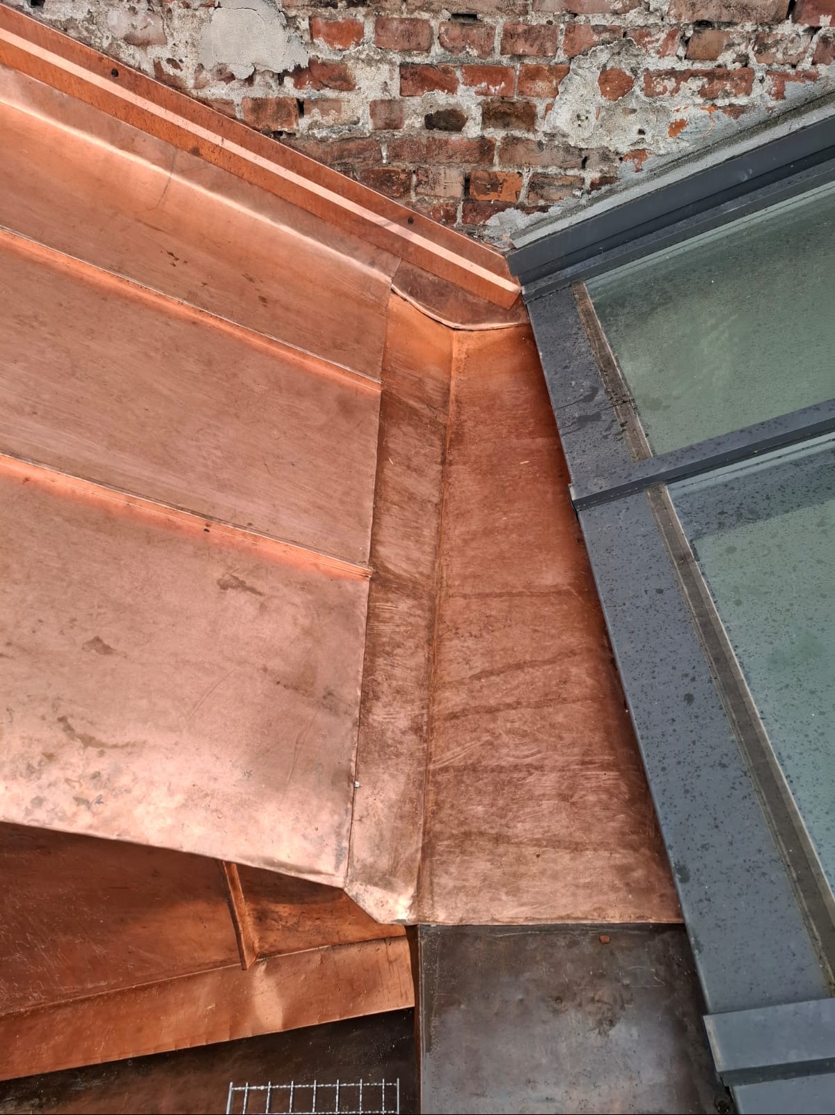 Miedziane orynnowanie dachu, detale łączenia z oknem dachowym i ceglaną ścianą. Widoczne ślady patyny na miedzi.