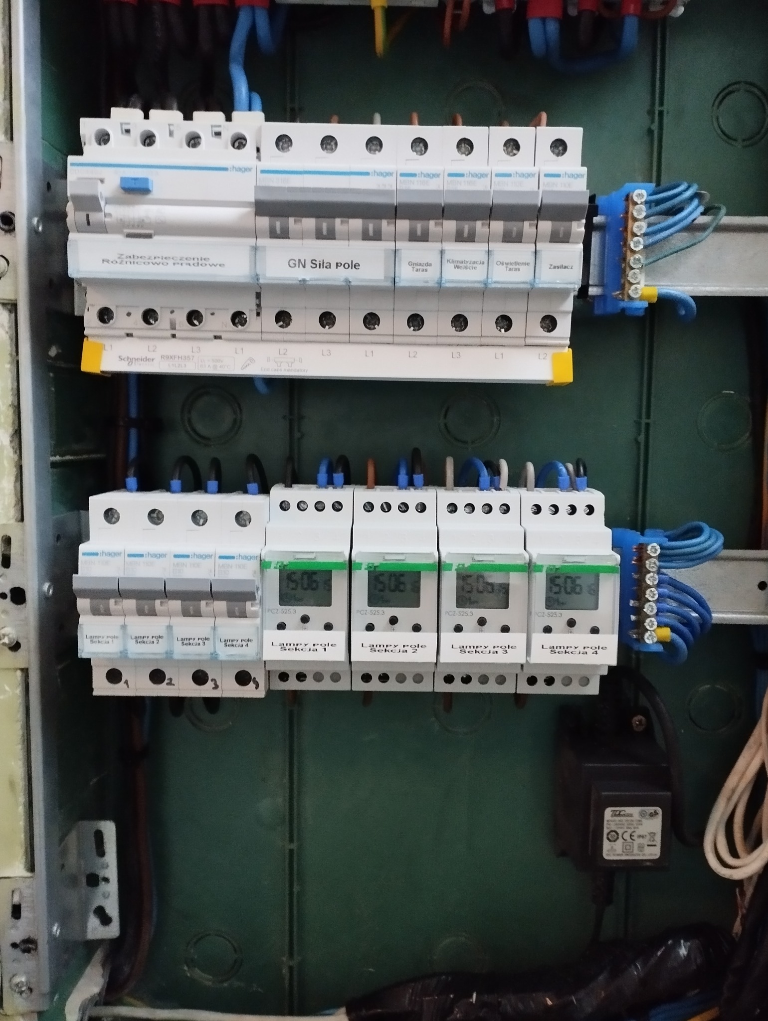 Rozdzielnia elektryczna z zabezpieczeniami różnicowoprądowymi Schneider i programatorami czasowymi Hager, widoczne przewody i listwy zaciskowe.