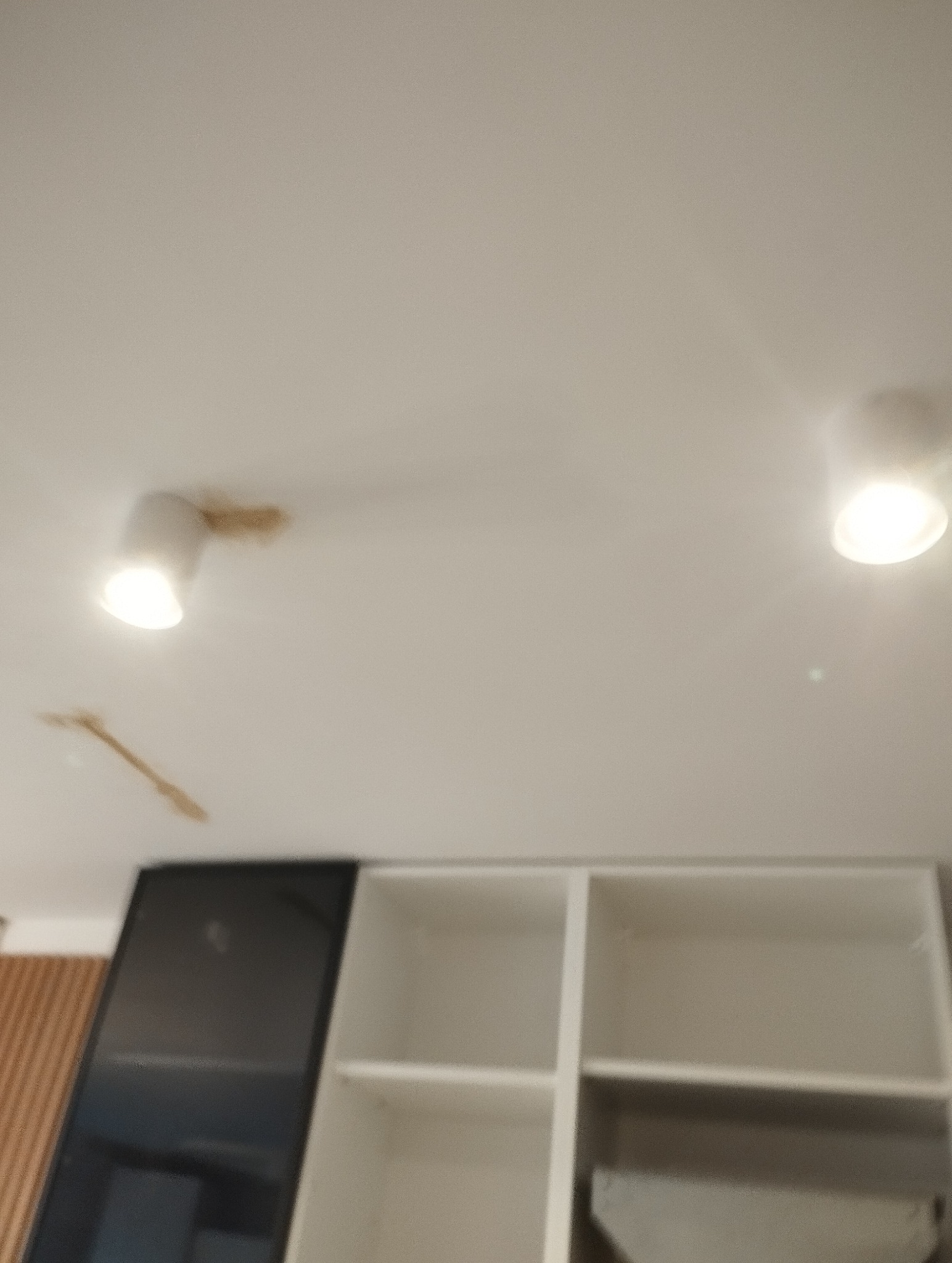 Dwa punkty oświetleniowe sufitowe, zamontowane nad zabudową meblową w jasnym wnętrzu. Widoczne ślady po montażu lamp.