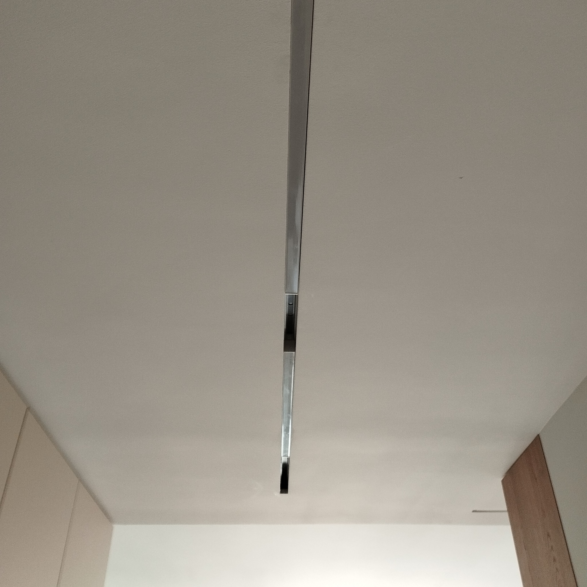 Nowoczesne oświetlenie szynowe, minimalistyczny design. Srebrna szyna z czarnymi reflektorami zamontowana na białym suficie. Widok z dołu, fragment ściany i szafki.