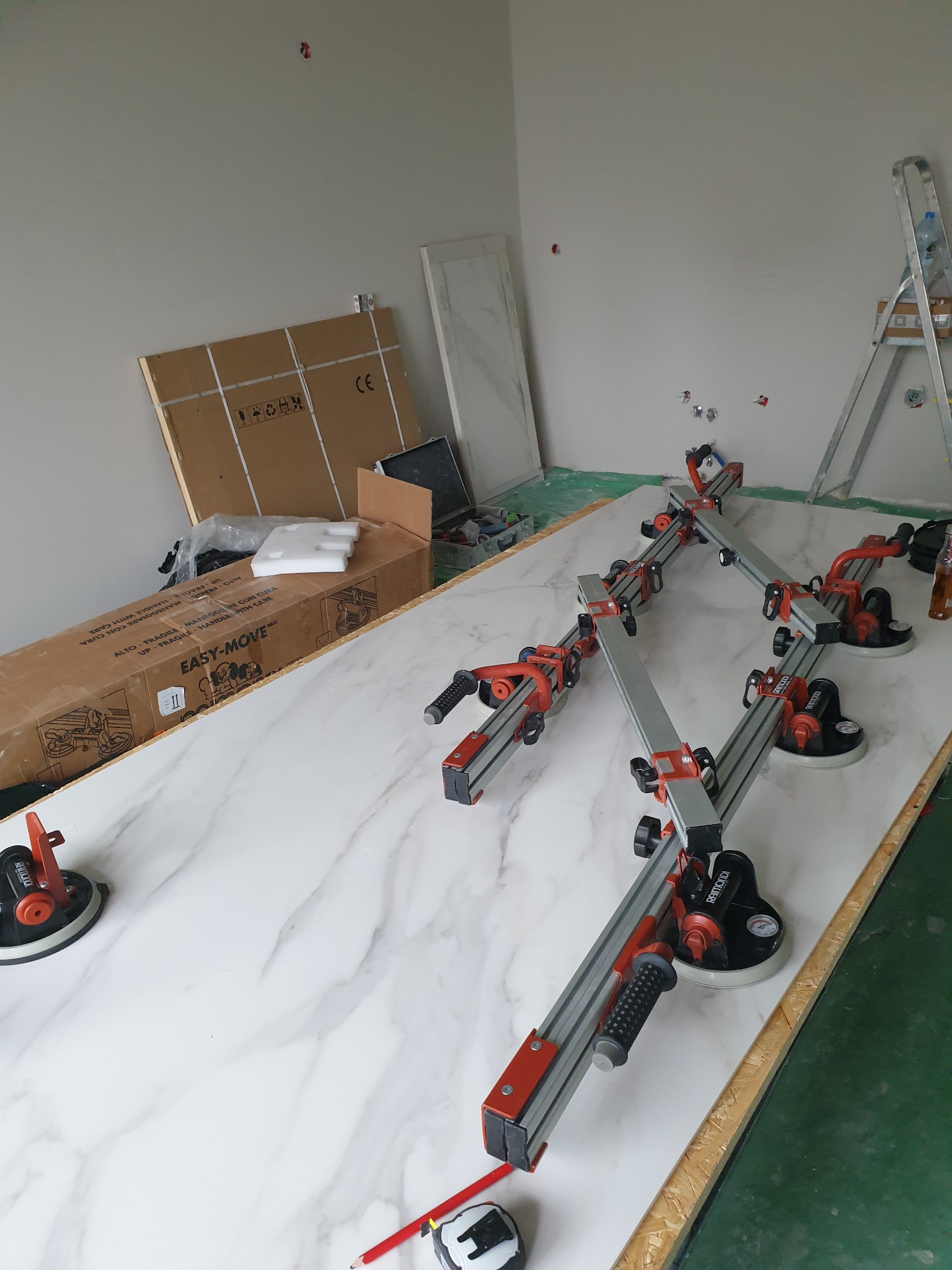 Marmurowa płyta na stole roboczym z przyssawkami i systemem szyn Raimondi Easy-Move, przygotowywana do montażu w łazience, widoczna kartonowa paczka z napisem EASY-MOVE