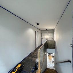 Jakub Ponc - Świeżo pomalowany korytarz z zabezpieczonymi powierzchniami taśmą malarską i folią, widoczny laserowy niwelator DeWalt, przygotowany do dalszych prac wykończeniowych.