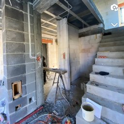 Jakub Ponc - Wnętrze w trakcie murowania ścian z bloczków betonowych, widoczne instalacje elektryczne w peszlach, prowizoryczne schody betonowe i narzędzia pracy.