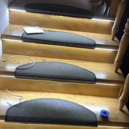 Jakub Ponc - Montaż dywanowych nakładek na drewnianych schodach z podświetleniem LED, widoczne narzędzia do cięcia kabli i fragment stopy