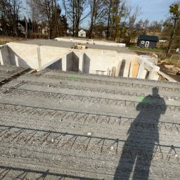 Jakub Ponc - Fundamenty domu jednorodzinnego w trakcie budowy, widoczne zbrojenia i ściany fundamentowe z bloczków betonowych, cień osoby fotografującej na pierwszym planie.