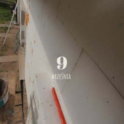 Jakub Ponc - Fragment ściany budynku z nałożonymi płytami izolacyjnymi, widoczny poziomica i data '9 września' nałożona cyfrowo na obraz.