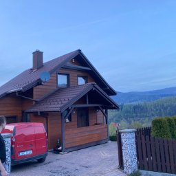 Jakub Ponc - Drewniany dom jednorodzinny z czerwoną furgonetką zaparkowaną przed garażem, widok na góry w tle, pochmurne niebo.