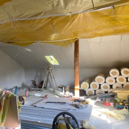 Jakub Ponc - Poddasze w trakcie ocieplania i montażu płyt karton gips, widoczne rolki wełny mineralnej, płyty gipsowe, drabina i narzędzia, folia paroizolacyjna pod dachem.