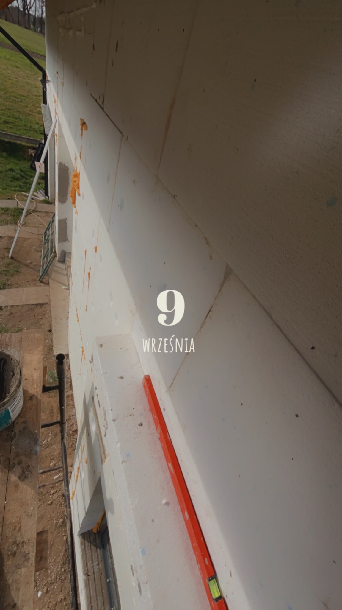 Fragment ściany budynku z nałożonymi płytami izolacyjnymi, widoczny poziomica i data '9 września' nałożona cyfrowo na obraz.