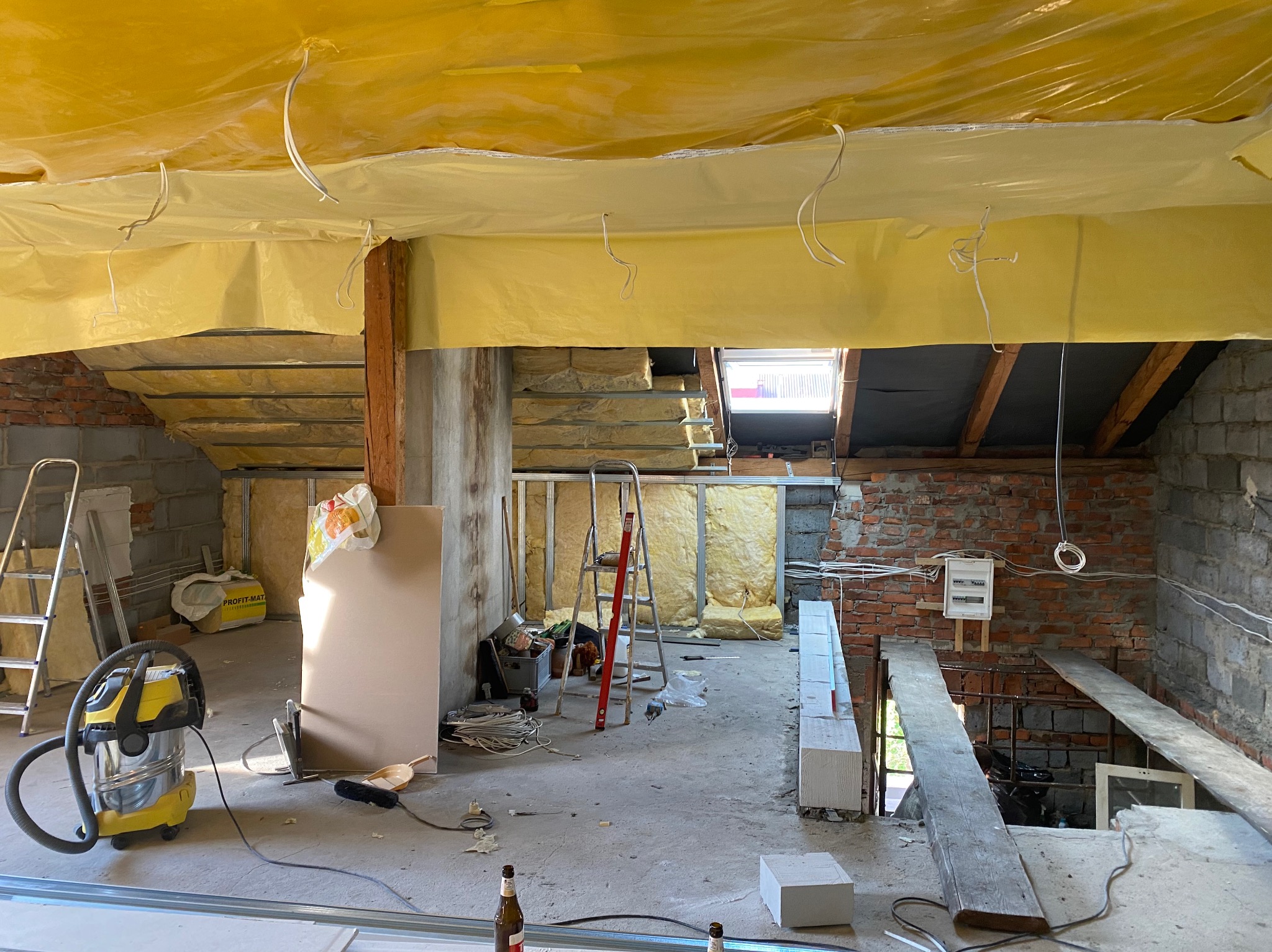 Poddasze w trakcie prac w Brennej: widoczne ocieplenie folią, wełna mineralna, fragmenty murowanej ściany, instalacja elektryczna, drabina i narzędzia pracy.