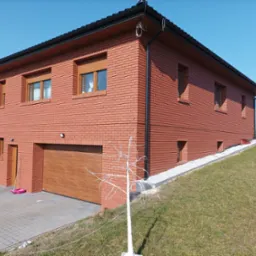 Nowoczesny dom z cegły klinkierowej, z garażem z drewnianą bramą, schodami wejściowymi i minimalistyczną dekoracją w ogrodzie, w słoneczny dzień.