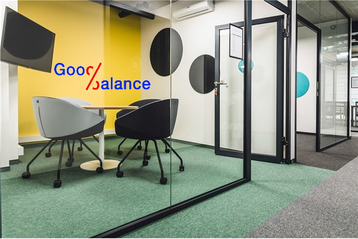 Nowoczesne biuro z przeszklonymi ścianami, żółtą ścianą z okrągłymi dekoracjami, okrągłym stołem i dwoma krzesłami na kółkach, zielona wykładzina dywanowa.