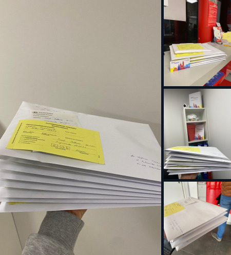 Stos białych kopert z żółtymi formularzami, trzymany w dłoni, z widocznymi adresami i danymi, w tle fragment biura z regałem i materiałami promocyjnymi.