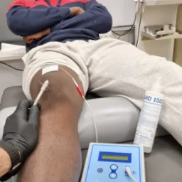 Elektroterapia igłowa kolana pacjenta z użyciem urządzenia Epte O-electrólisis percutánea terapéutica, widoczny żel do dezynfekcji skóry AHD 1000.