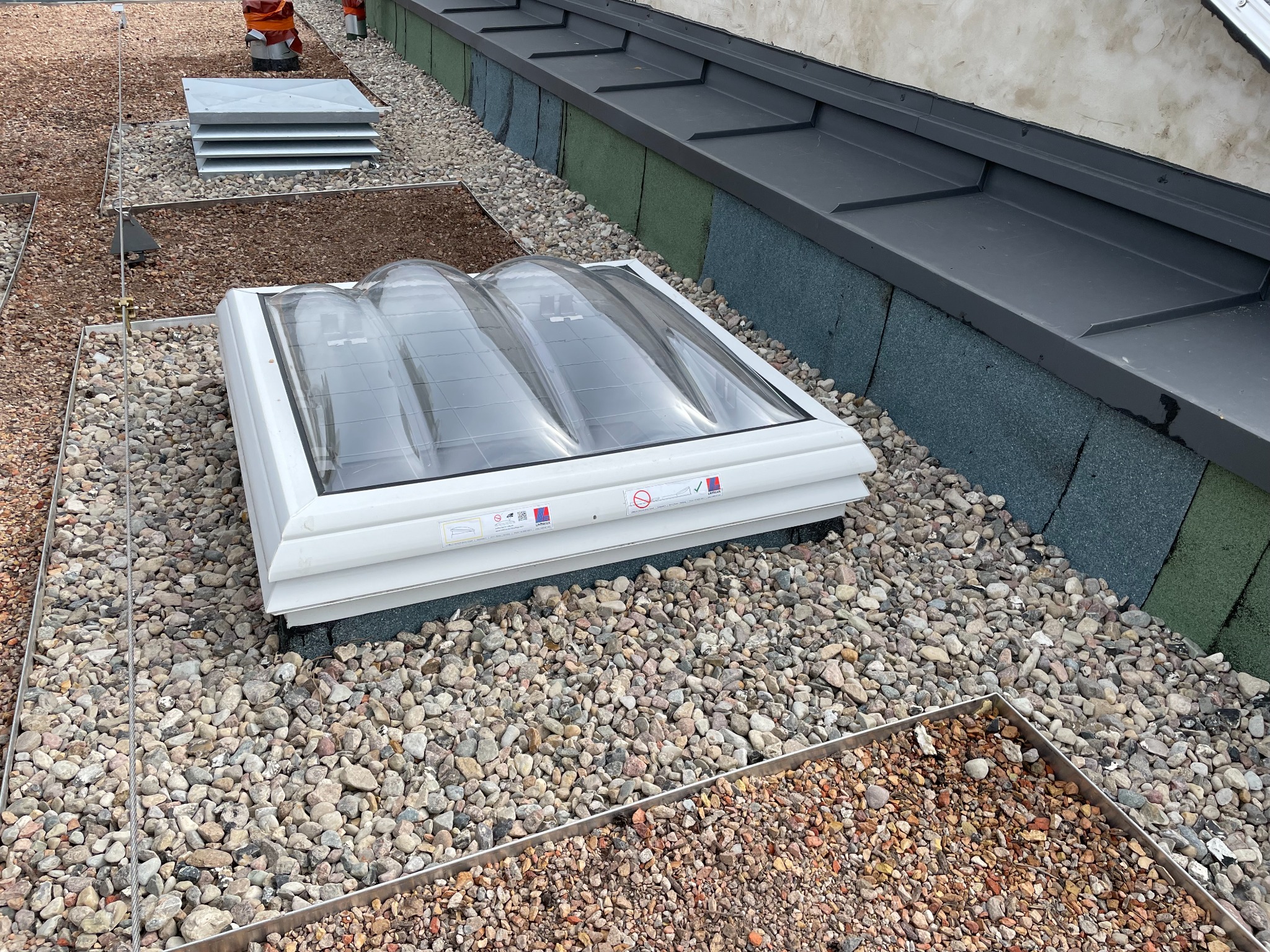 Płaski dach pokryty drobnymi kamieniami, z zamontowanym świetlikiem dachowym o trzech kopułach i systemem odgromowym z metalowych linek.