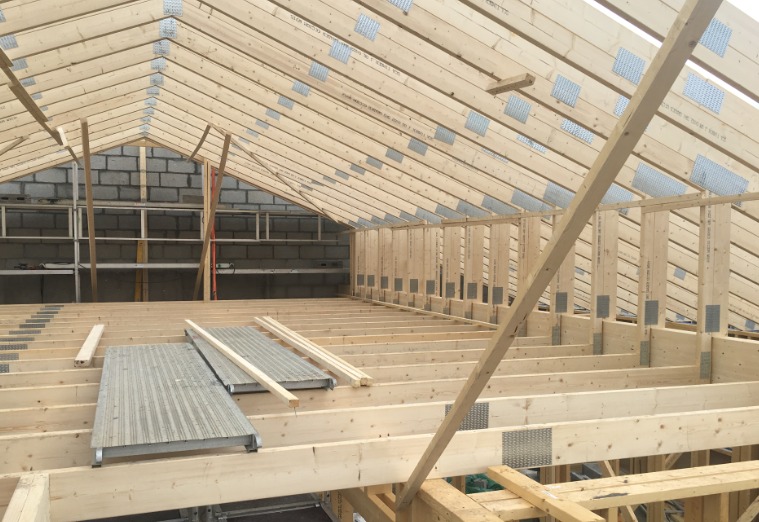 Konstrukcja drewniana dachu w trakcie budowy, widoczne krokwie, płyty łączące, ściany z bloczków betonowych oraz podesty robocze.