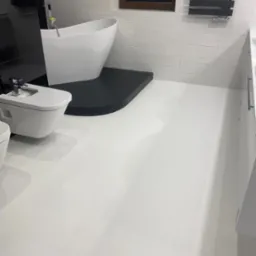 Nowoczesna łazienka z białą, jednolitą podłogą, czarną platformą pod wanną wolnostojącą i grzejnikiem drabinkowym na ścianie z białych płytek.