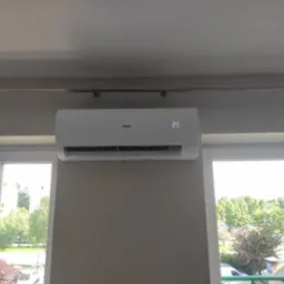 Biały klimatyzator Haier zamontowany na ścianie nad oknem z widokiem na zieleń miejską, wyświetlający temperaturę 23 stopnie.