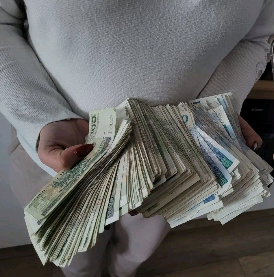 Osoba w jasnym swetrze trzyma w dłoniach duży plik banknotów polskich złotych o nominałach 50 i 100 zł.