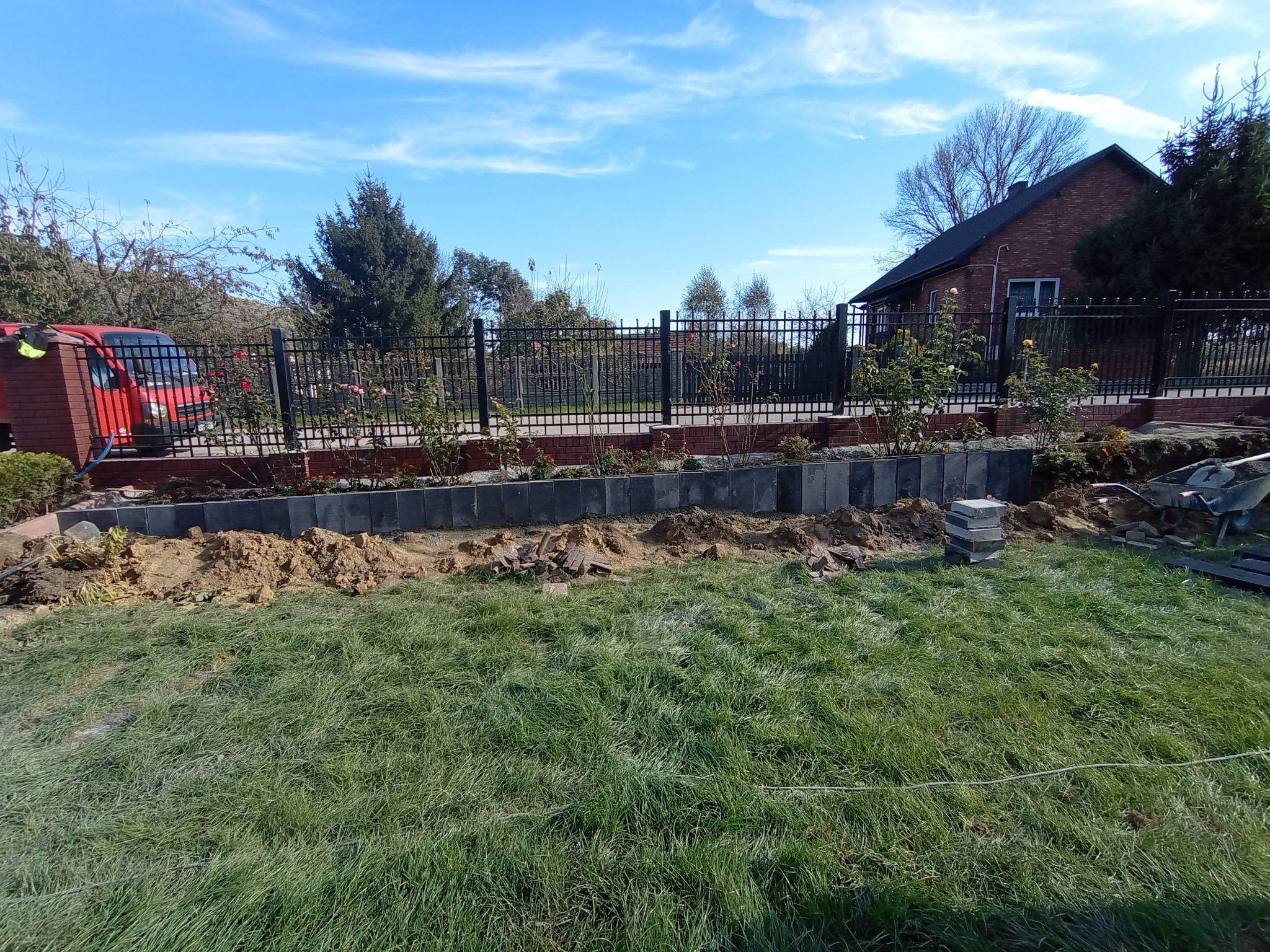 W Skalbmierzu trwa budowa ogrodzenia z metalową siatką na podmurówce z betonowych bloczków. Widoczny fragment ogrodu z przygotowanym podłożem i stosem bloczków.