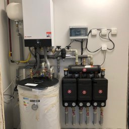 BWA Usługi Hydrauliczne - Zmontowana instalacja grzewcza z kotłem Viessmann, zasobnikiem ciepłej wody w folii i rozdzielaczem z pompami obiegowymi. Widoczne rury, zawory i skrzynka elektryczna.