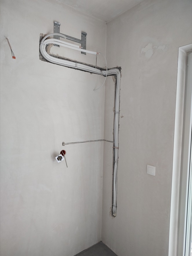 Wewnętrzna instalacja rur i przewodów, prawdopodobnie pod system rozprowadzania chłodnego powietrza, zamontowana na ścianie w surowym stanie wykończenia, widoczne uchwyty mocujące i puszka...