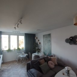 Chaykovskyy Group uslugi remontowe - Jasne wnętrze salonu z parkietem ułożonym w jodełkę, szarą sofą z poduszkami, białym stolikiem kawowym i dekoracjami ściennymi.