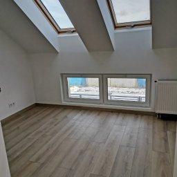 Firma Dorota Stalpińska - Poddasze z drewnopodobną podłogą, dwoma oknami dachowymi i grzejnikiem, świeżo po remoncie.
