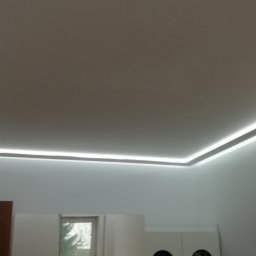 Firma Dorota Stalpińska - Biały sufit z zamontowanym oświetleniem LED wzdłuż krawędzi, widoczny fragment drzwi i okno w tle.